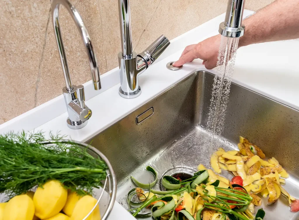person turning on the garbage disposal on a modern sink to shred up the food waste